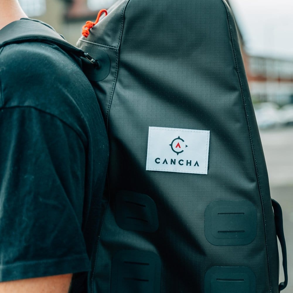 A person wearing a black T-shirt carries a lightweight, water-repellent Original Racquet Bag (25L) by Cancha on their shoulder.