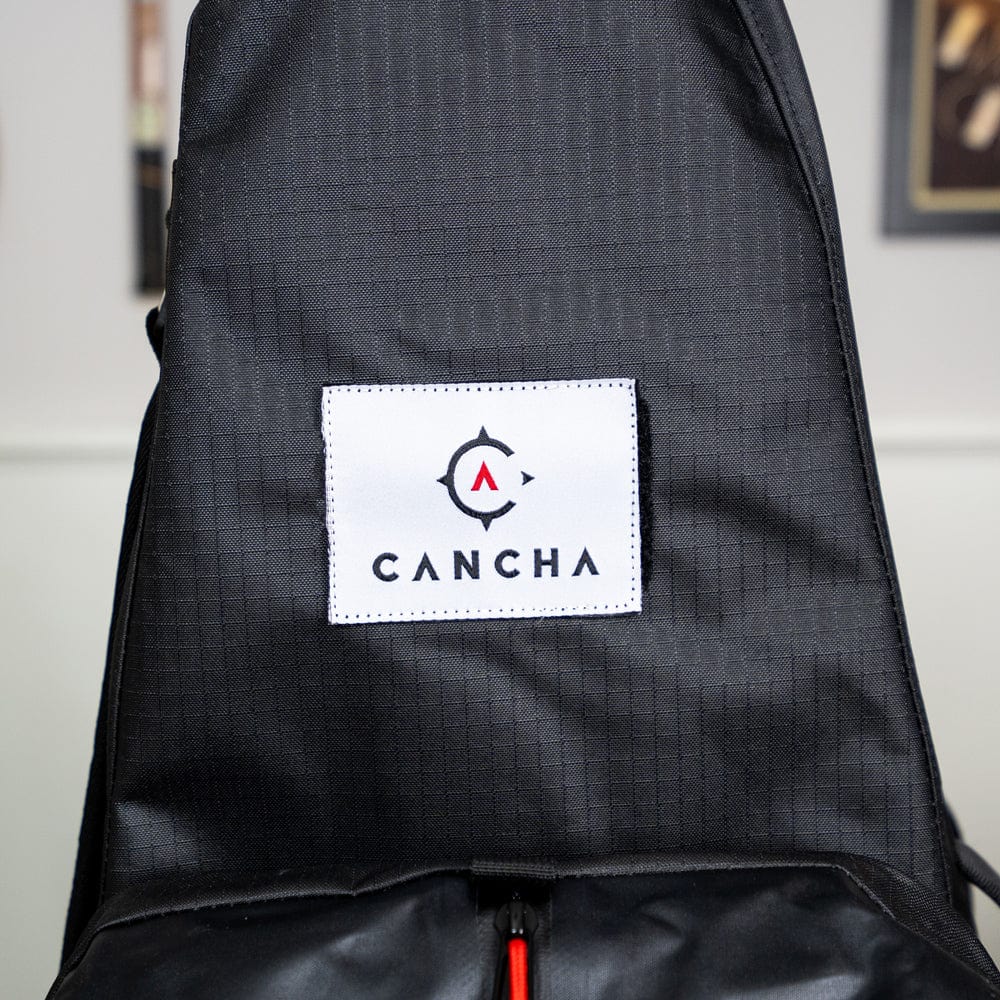 Close-up of the Original Racquet Bag (25L) by Cancha, showcasing its grid pattern fabric and a white patch featuring the "Cancha" logo at the center, crafted from lightweight water-repellent materials.