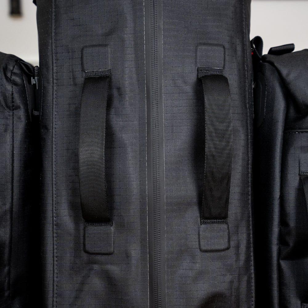 Close-up of black handles on a vertically aligned Cancha Original Racquet Bag (25L) with visible zippers and textured fabric crafted from lightweight, water-repellent materials.