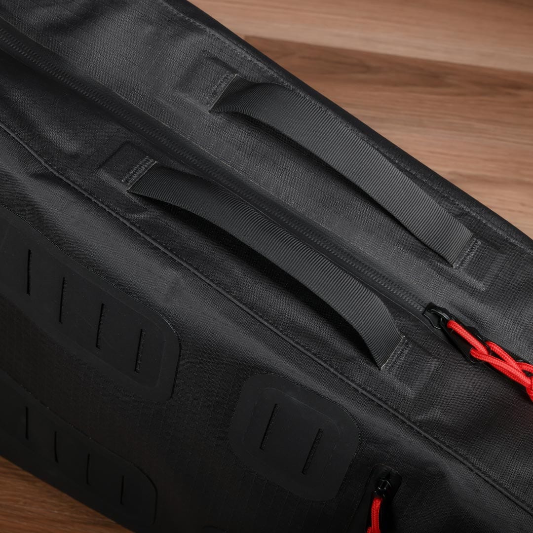 A close-up of the Cancha Racquet Bag Voyager on a wooden surface, showcasing its dual handles, rugged fabric texture, red zipper pull, and weatherproof materials.