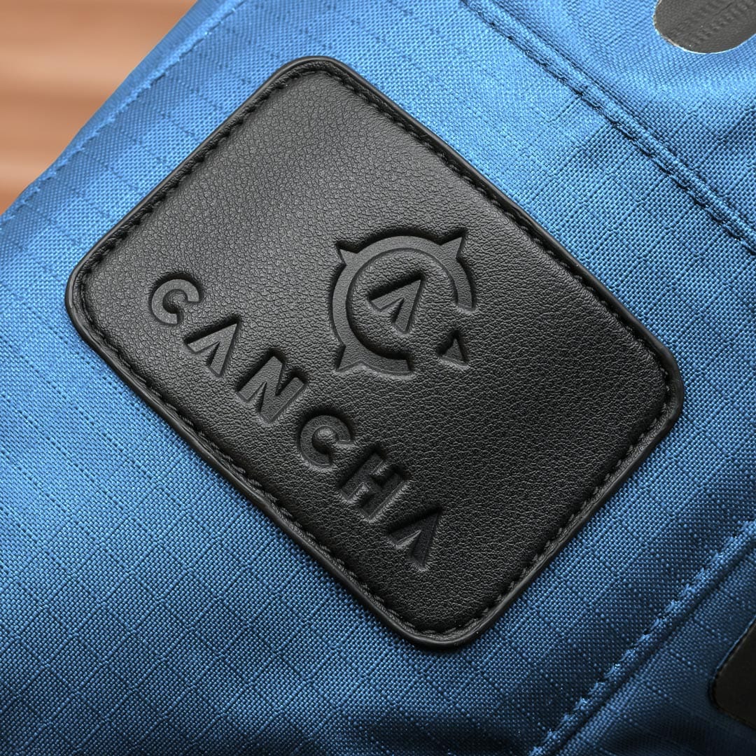 Close-up of a blue Racquet Bag Voyager made from weatherproof materials, featuring a black leather patch with the embossed logo and text "Cancha".