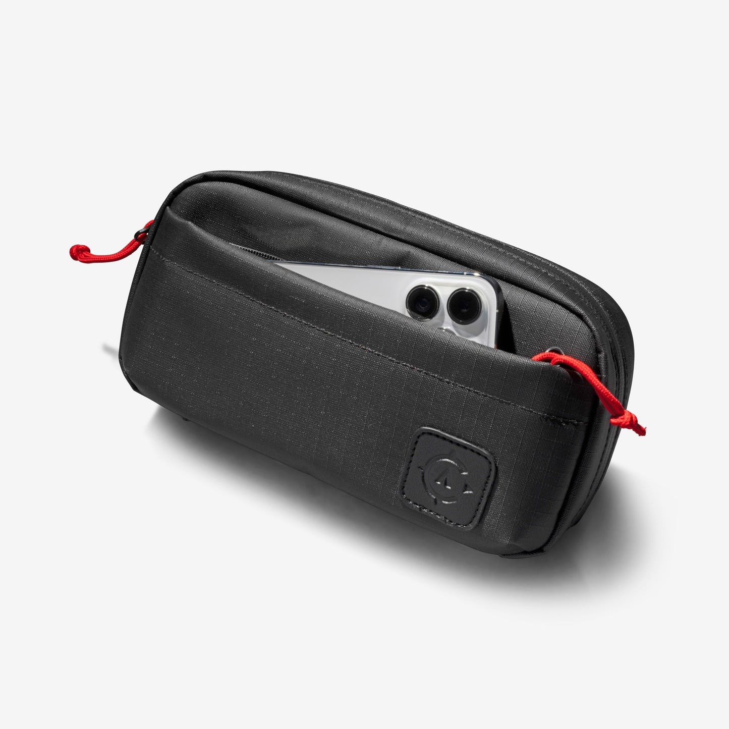 A black zippered pouch with a red drawstring, partially open to reveal a smartphone inside, showcases the adaptable design of Cancha's Sling Bag.